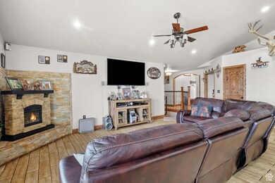 Living area featuring arched walkways, ceiling fan, wood finished floors, lofted ceiling, and a stone fireplace
