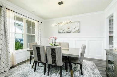 Dining area featuring a decorative wall, dark wood-type flooring, crown molding, wainscoting, and wine cooler