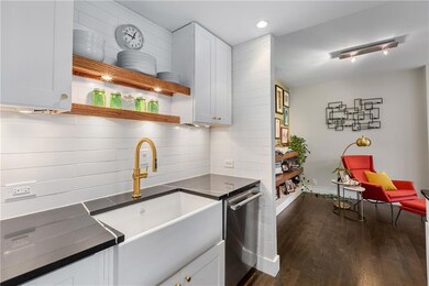 Kitchen featuring stainless steel dishwasher, dark countertops, dark wood-style flooring, white cabinetry, and tasteful backsplash
