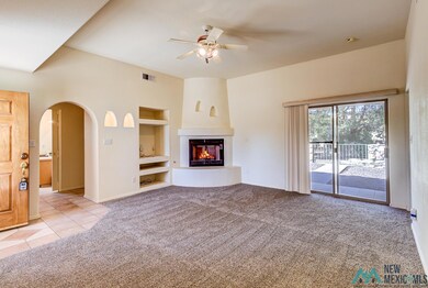 Unfurnished living room with built in features, light carpet, arched walkways, a glass covered fireplace, and a ceiling fan
