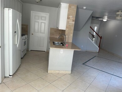 Kitchen featuring white appliances, decorative backsplash, light tile patterned flooring, light stone countertops, and white cabinets