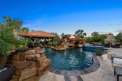 Pool at dusk featuring an outdoor stone fireplace, a gazebo, a patio, and a pool with connected hot tub