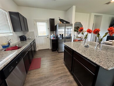 Kitchen featuring dark wood finished floors, appliances with stainless steel finishes, backsplash, a center island, and light stone countertops