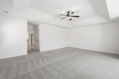 Spare room featuring a raised ceiling, light colored carpet, and ceiling fan