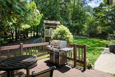 Deck with grilling area, a lawn, a playground, and view of scattered trees