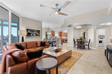 Living room featuring a wall of windows, light tile patterned floors, baseboards, washer / clothes dryer, and ceiling fan with notable chandelier- Virtually Edited