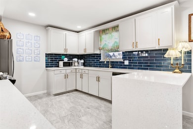 Kitchen featuring white cabinets, tasteful backsplash, light stone countertops, freestanding refrigerator, and white microwave