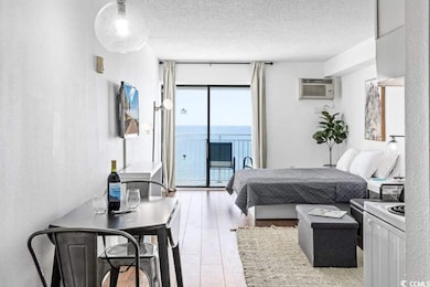 Bedroom with light wood-style flooring, a textured ceiling, access to outside, a wall mounted AC, and a textured wall