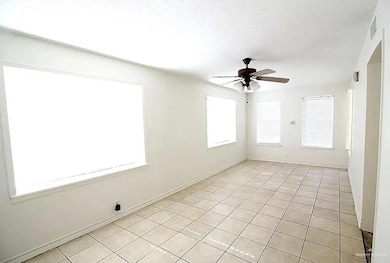 Empty room with ceiling fan, light tile patterned flooring, and a textured ceiling