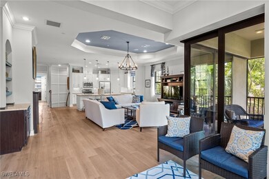 Living room featuring ornamental molding, a tray ceiling, a chandelier, light wood-style floors, and recessed lighting