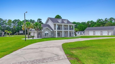View of front of house featuring stone siding, a front yard, a balcony, and driveway