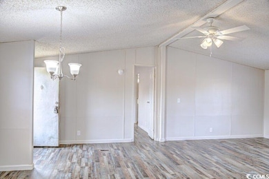 Empty room with wood finished floors, a ceiling fan, a textured ceiling, a chandelier, and lofted ceiling