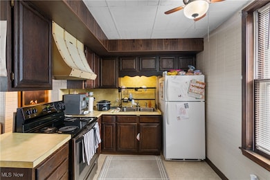 Kitchen with range with electric stovetop, dark brown cabinetry, freestanding refrigerator, light countertops, and under cabinet range hood
