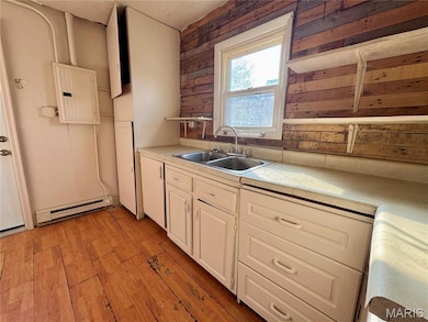 Kitchen with electric panel, light countertops, wood walls, a baseboard radiator, and light wood finished floors