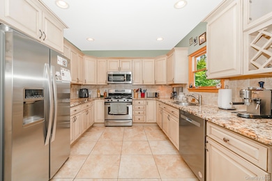 Kitchen with appliances with stainless steel finishes, cream cabinetry, light stone countertops, decorative backsplash, and recessed lighting
