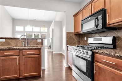 Kitchen featuring gas range, dark stone countertops, decorative backsplash, decorative light fixtures, and brown cabinets