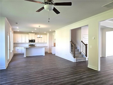 Kitchen featuring crown molding, open floor plan, white cabinets, a center island with sink, and dark wood finished floors