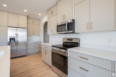 Kitchen with appliances with stainless steel finishes, cream cabinetry, light wood finished floors, recessed lighting, and light stone countertops