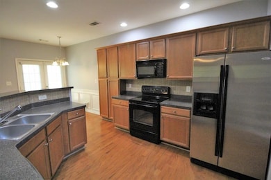 Kitchen with black appliances, dark countertops, backsplash, light wood-style flooring, and brown cabinets