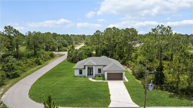 View of front facade with concrete driveway, a front yard, a wooded view, a garage, and stucco siding