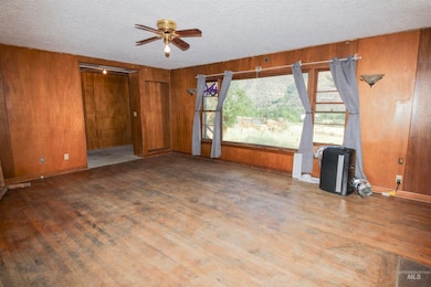 Unfurnished living room featuring wooden walls, wood finished floors, ceiling fan, and a textured ceiling