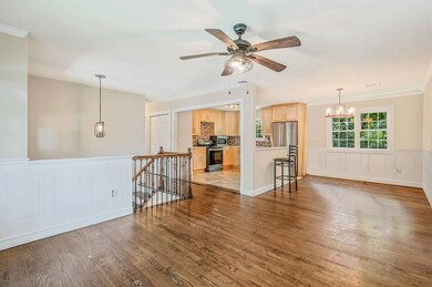 Unfurnished living room with a chandelier, a ceiling fan, dark wood-type flooring, a wainscoted wall, and a decorative wall
