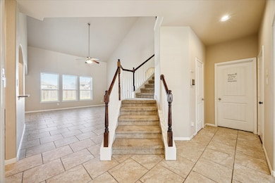 This bright and spacious entryway features tiled flooring and a staircase with wooden railings leading to the second floor. The open layout connects to a living area with large windows, providing plenty of natural light.