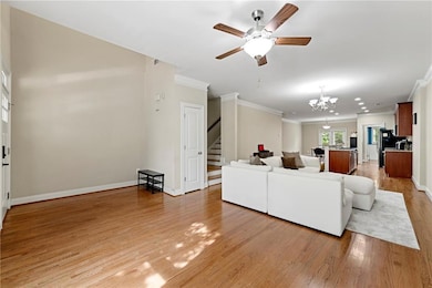 Living room featuring stairs, light wood-type flooring, ornamental molding, ceiling fan, and a chandelier