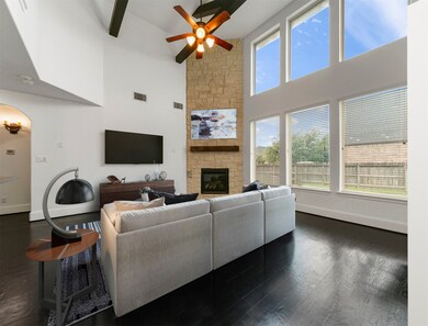 This lovely living room is open and bright! Featuring soaring high ceilings with wood beams, a ceiling fan, beautiful dark stained wood floors, an elegant mantle and fire place, large wall of windows providing a beautiful view of the backyard, and tons of natural light in throughout the day!