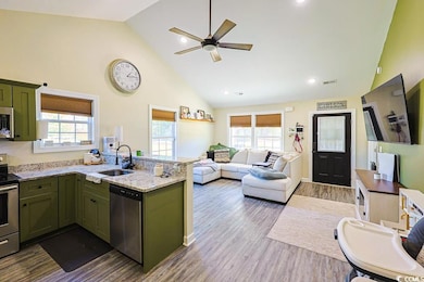 Kitchen with green cabinets, high vaulted ceiling, a peninsula, light stone counters, and stainless steel appliances