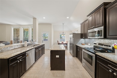 Large Kitchen with dark brown cabinets, stainless steel appliances, a kitchen island, decorative light fixtures, and light tile patterned floors