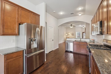 Kitchen featuring tasteful backsplash, stainless steel appliances, light stone countertops, brown cabinetry, and a peninsula