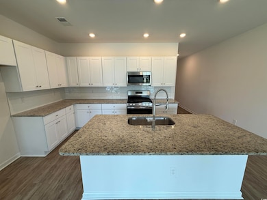 Kitchen featuring light stone countertops, white cabinetry, backsplash, appliances with stainless steel finishes, and dark wood-style flooring