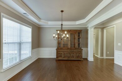 Unfurnished dining area featuring dark wood finished floors, decorative columns, a chandelier, a wainscoted wall, and a decorative wall