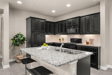 Kitchen with dark cabinetry, recessed lighting, black appliances, light tile patterned flooring, and light stone counters