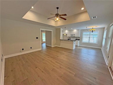 Unfurnished living room with healthy amount of natural light, ceiling fan, a chandelier, recessed lighting, and light wood-style floors