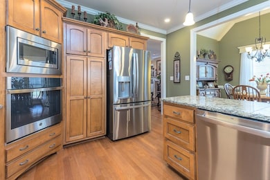 Kitchen with brown cabinets, stainless steel appliances, light wood finished floors, hanging light fixtures, and crown molding