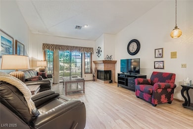 Living area featuring light wood-style flooring, a fireplace, lofted ceiling, and a textured ceiling