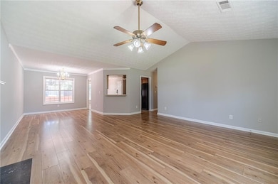 Unfurnished living room with a chandelier, ceiling fan, light wood finished floors, baseboards, and a textured ceiling