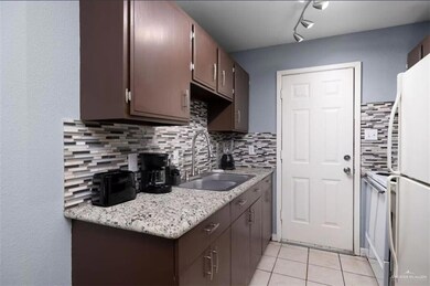 Kitchen with light countertops, freestanding refrigerator, light tile patterned floors, backsplash, and dark brown cabinets