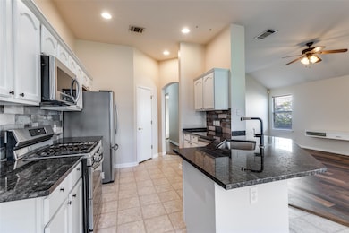 Kitchen featuring stainless steel appliances, backsplash, lofted ceiling, white cabinets, and a peninsula