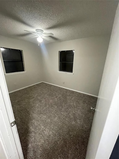 Empty room with a textured ceiling, ceiling fan, and dark carpet