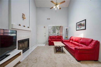 Tiled living area featuring a high ceiling, ceiling fan, a fireplace, and baseboards