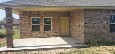Doorway to property featuring brick siding, a patio area, and a shingled roof