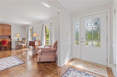 Entrance foyer with ornamental molding, light wood-style flooring, and plenty of natural light