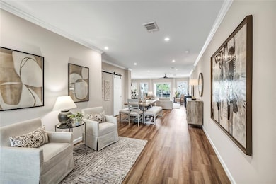 Living room featuring a barn door, ornamental molding, wood finished floors, and recessed lighting