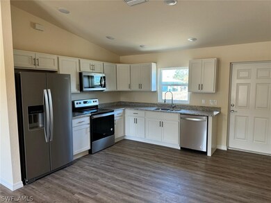 Kitchen featuring stainless steel appliances, sink, white cabinets, and lofted ceiling