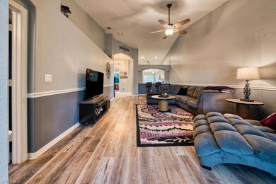 Living area with arched walkways, high vaulted ceiling, light wood finished floors, a textured wall, and ceiling fan