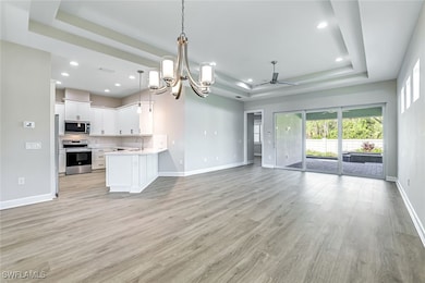 Unfurnished living room with a chandelier, a raised ceiling, light wood-style floors, a ceiling fan, and recessed lighting