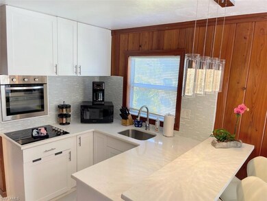 Kitchen with appliances, white cabinetry, backsplash, a peninsula, and light stone countertops